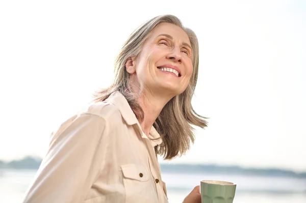 Glanzende vrouw met kopje op zoek naar buiten — Stockfoto