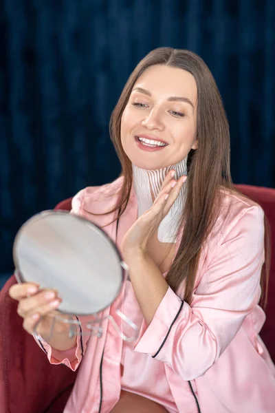 Молода жінка в рожевій білизні і зі стрічками на шиї дивиться у дзеркало — стокове фото