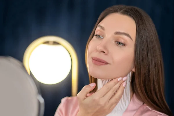 Ung kvinna i rosa underkläder och med band på halsen tittar i spegeln — Stockfoto