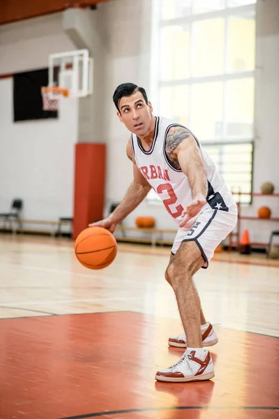 Dark-haired athletic man playing basket-ball in the gym — Stock Photo, Image