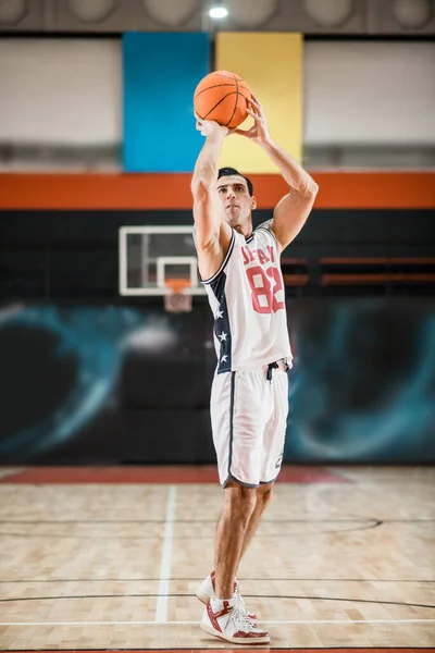 Ung atletisk mann i hvit sportsdrakt spiller basket-ball i gymsalen – stockfoto