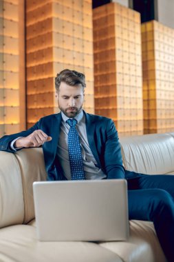 Takım elbiseli sakallı bir adam dizüstü bilgisayarda çalışıyor ve konsantre görünüyor.