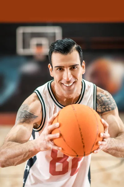 Brunette handsome sportsman holding a big orange ball in hands — Stock Photo, Image