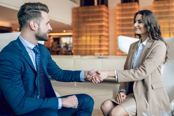 Woman in a beige suit shaking hands with her business partner