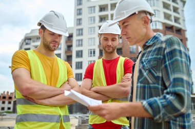 Teknik çizimleri analiz eden üç kafkas işçisi.