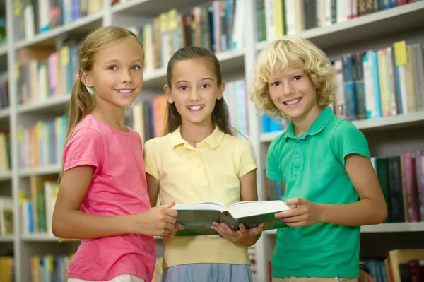 Trois camarades de classe posant pour la caméra dans une bibliothèque publique — Photo