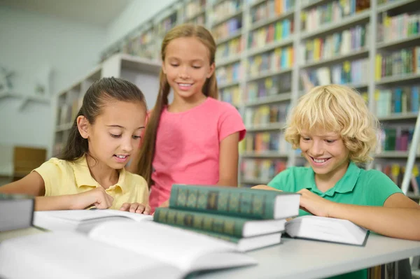Tre söta klasskamrater studerar tillsammans på ett bibliotek — Stockfoto
