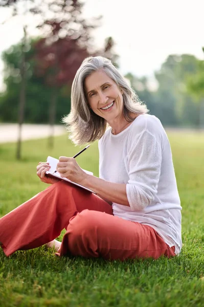 Femme souriante prenant des notes sur la pelouse — Photo