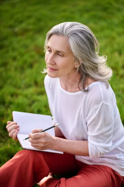 Grijsharige vrouw met notitieblok met pensive look — Stockfoto