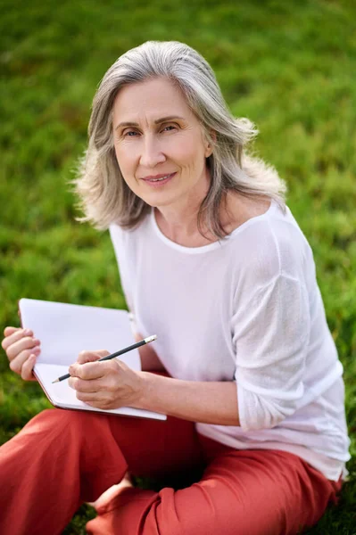 Vrouw met notitieboekje en potlood zittend op gras — Stockfoto