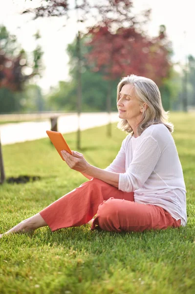 Kvinna tittar uppmärksamt på tablett sitter på gräsmattan — Stockfoto