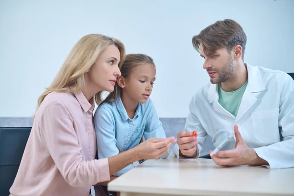 Male doctor demonstrating a deaf aid to his female patients