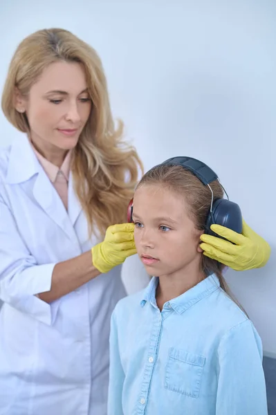 Otorrinolaringóloga mujer que pone auriculares a la niña en edad escolar —  Fotos de Stock