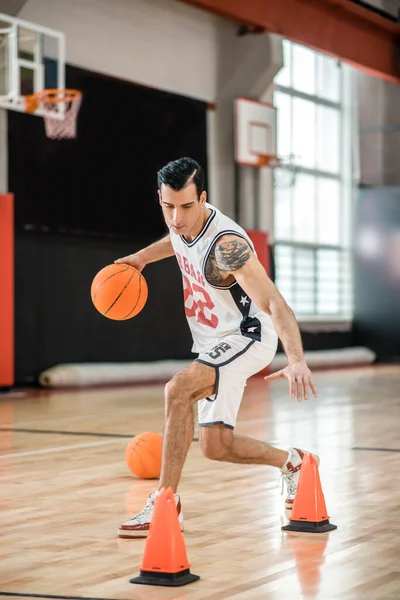 Getatoeëerde man in wit shportswear basketbal spelen en kijken betrokken — Stockfoto