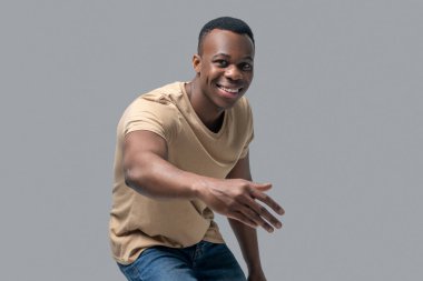 Koyu tenli, bej tişörtlü bir adamın stüdyo resmi.