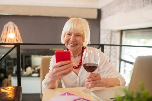 Elegantní starší žena si dává víno a mluví po telefonu — Stock fotografie