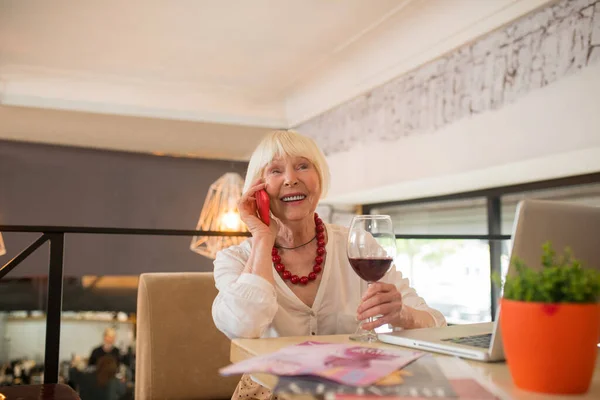 Sarışın kadın şarap içiyor ve telefonda konuşuyor. — Stok fotoğraf