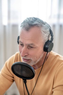 Kulaklıklı, gri saçlı bir adam internette ses konferansı veriyor.