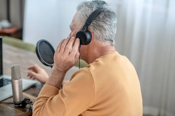 Egy ősz hajú férfi fülhallgatóban, aki online konferenciát tart. — Stock Fotó