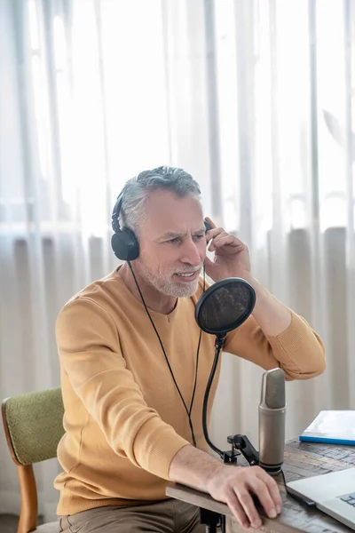 A gray-haired man in black headphones speaking in microphone and looking busy — Stock Photo, Image