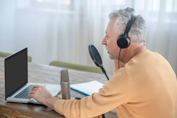 Un hombre de pelo gris con auriculares que tiene una conferencia de audio en línea —  Fotos de Stock
