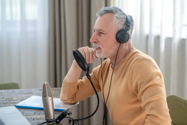 A gray-haired man in black headphones speaking in microphone and looking interetsed — Stock Photo, Image