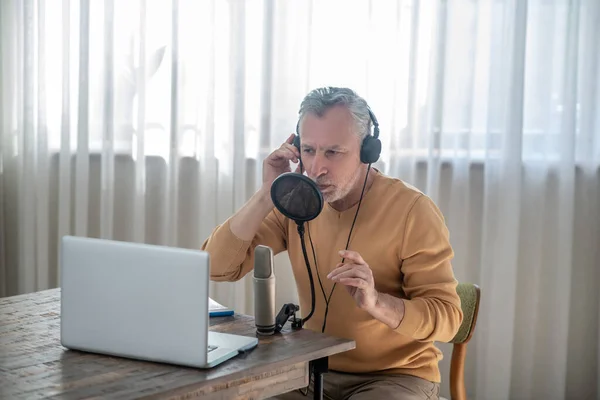 A gray-haired man in black headphones speaking in microphone and looking interetsed — Stock Photo, Image