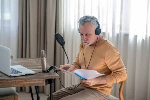 Een man met grijs haar in een zwarte koptelefoon die in een microfoon spreekt en er geïntereteerd uitziet. — Stockfoto