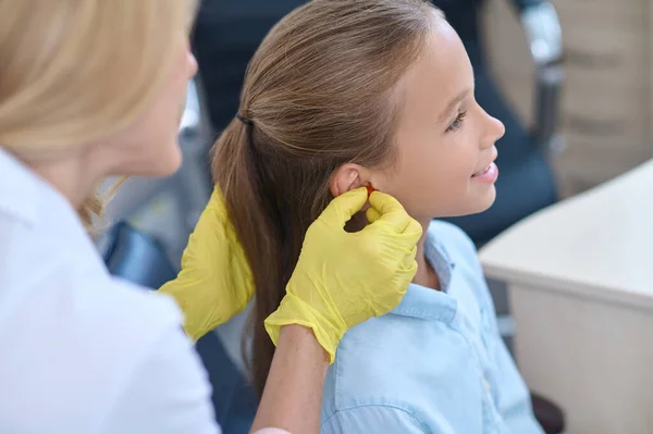 Otorrinolaringólogos manos cerca de la oreja de chica tranquila —  Fotos de Stock