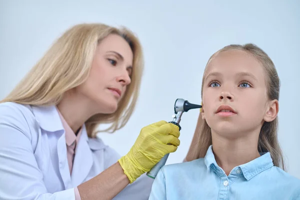 Chica tranquila y otorrinolaringólogo con otoscopio cerca de la oreja — Foto de Stock