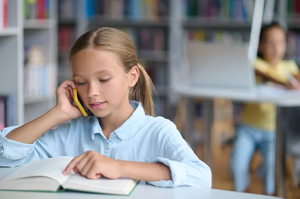 Akıllı telefonlu bir kız kütüphanede ders kitabını okuyor. — Stok fotoğraf