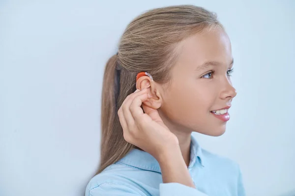 Profil dziewczyny dotykającej ucha aparatem słuchowym — Zdjęcie stockowe