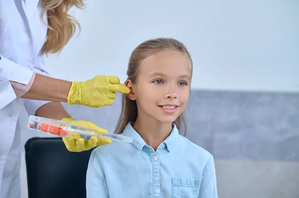 Uśmiechnięta dziewczyna i ręce otolaryngologa w pobliżu ucha — Zdjęcie stockowe