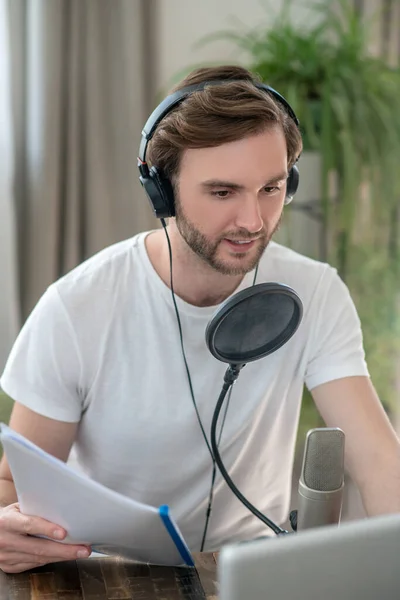 Joven barbudo sentado en auriculares y teniendo una conferencia de audio —  Fotos de Stock