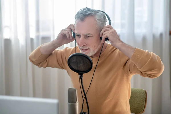 Egy ősz hajú férfi fekete fülhallgatóban, mikrofonban beszél. — Stock Fotó