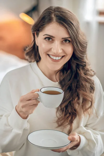 Mujer joven y bonita sentada en la cama y tomando café — Foto de Stock