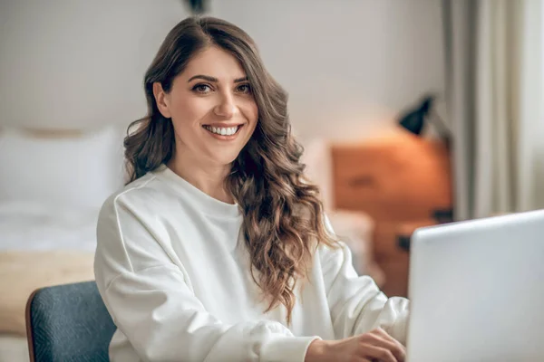 Elegante joven sentada a la mesa y trabajando en un portátil — Foto de Stock