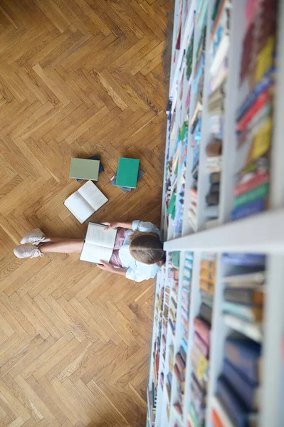 Школярка читає книгу на підлозі бібліотеки — стокове фото