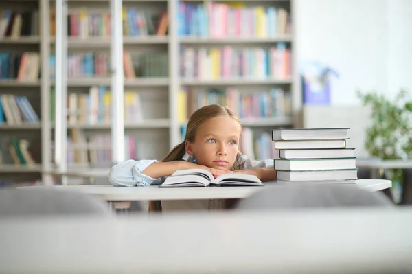 Flicka sittande vid bibliotekets skrivbord uttråkad — Stockfoto