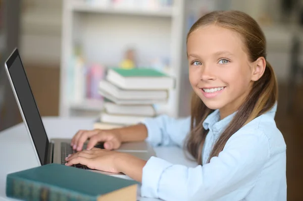 Menina bonito alegre trabalhando no laptop na biblioteca — Fotografia de Stock
