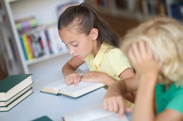 Två fokuserade skolbarn studerar tillsammans på biblioteket — Stockfoto