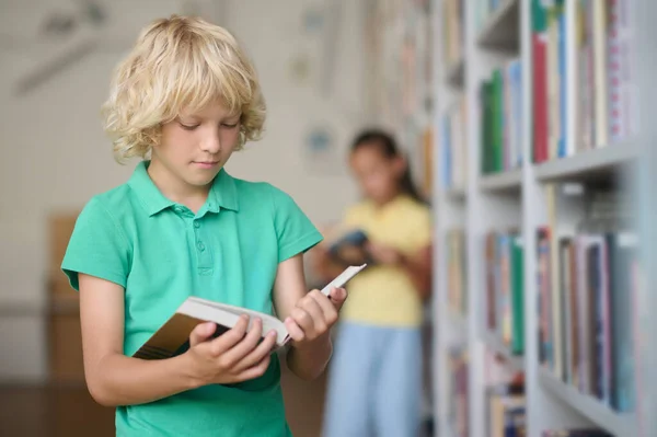 Poważny chłopak czyta podręcznik w jego rękach. — Zdjęcie stockowe