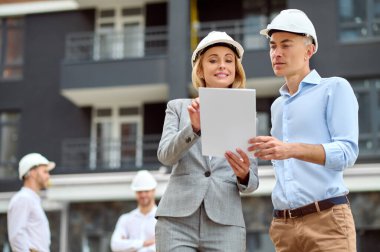 Gülümseyen bir yönetici ve bir erkek işçi seramik fayansı inceliyor.