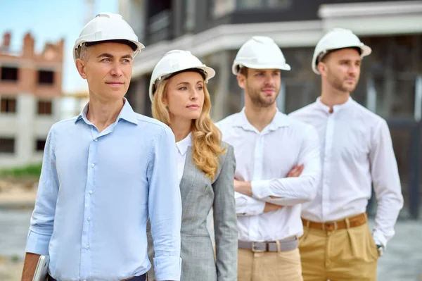 Cuatro personas adultas en sombreros de madera de pie en el sitio de construcción —  Fotos de Stock