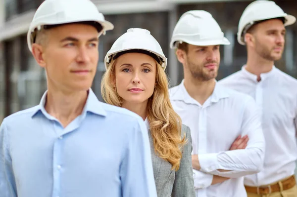 Woman supervisor and builders in hardhats standing outdoors — Stock Photo, Image