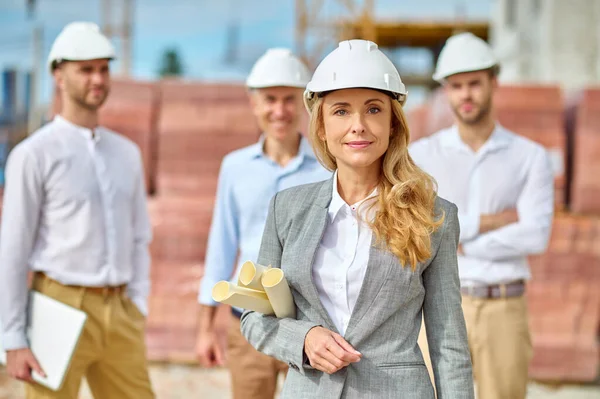 Confident serene blonde inspector with building plans standing outdoors