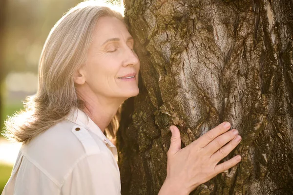 Volwassen lachende vrouw leunend tegen boom — Stockfoto