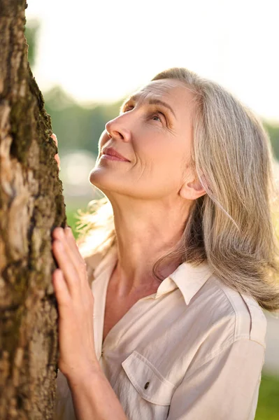 Glimlachende vrouw kijkt gepensioneerd omhoog naar boom — Stockfoto