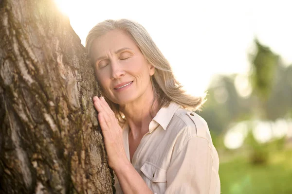 Vrouw met hangende oogleden leunend tegen een boom — Stockfoto