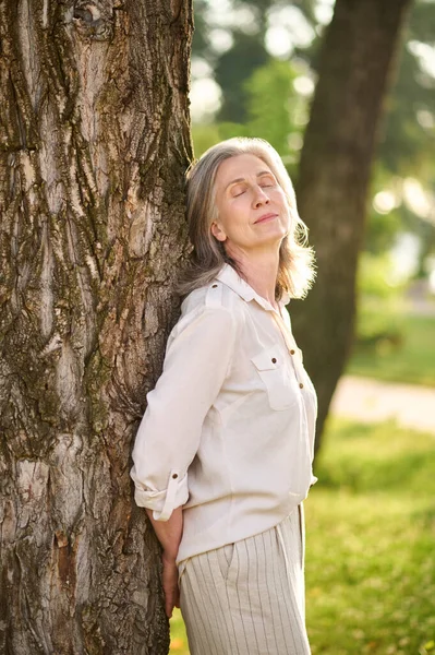 Жінка спирається на дерево в оптимістичному настрої — стокове фото